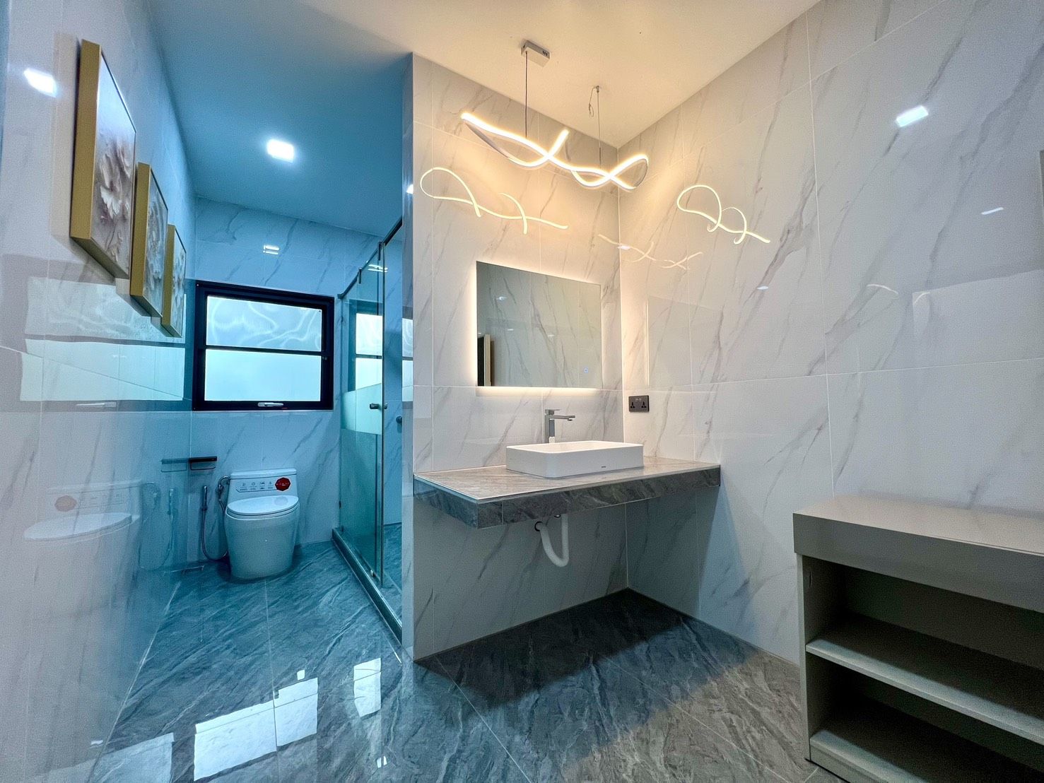 Un baño moderno con cabina de ducha de vidrio, un lavabo blanco y suelo de mármol.