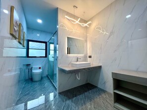 A modern bathroom with a glass shower enclosure, a white sink, and a marble floor.