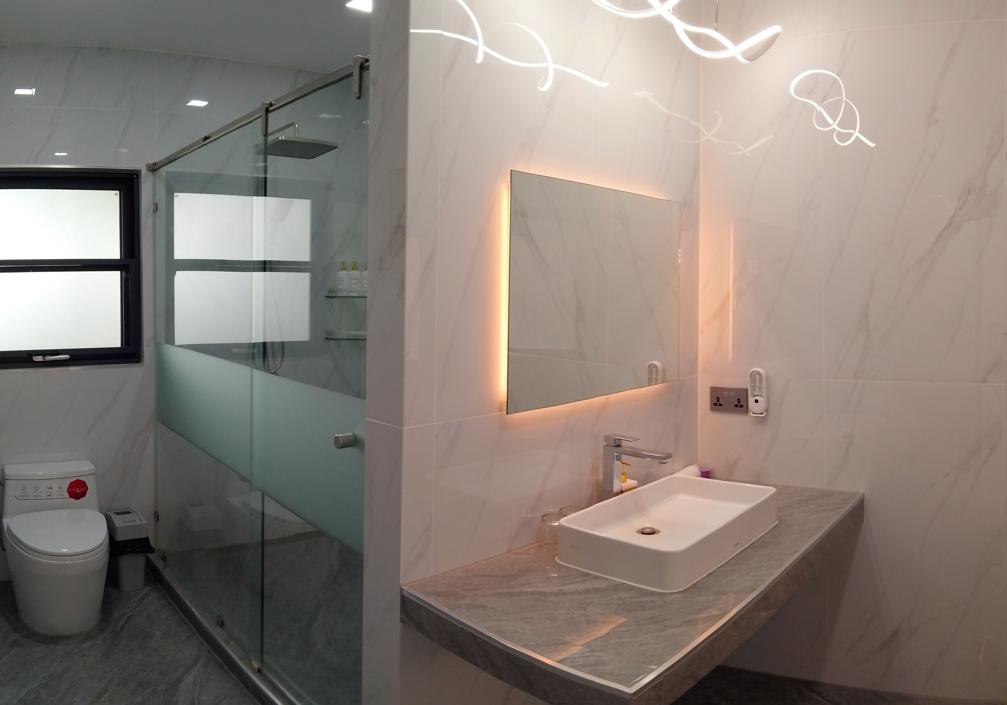 Une salle de bain moderne avec une douche à parois de verre, un lavabo en marbre et un miroir fixé au mur.