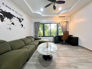 A modern living room with a sectional sofa, a round coffee table, a desk with a chair, and a large window with curtains.