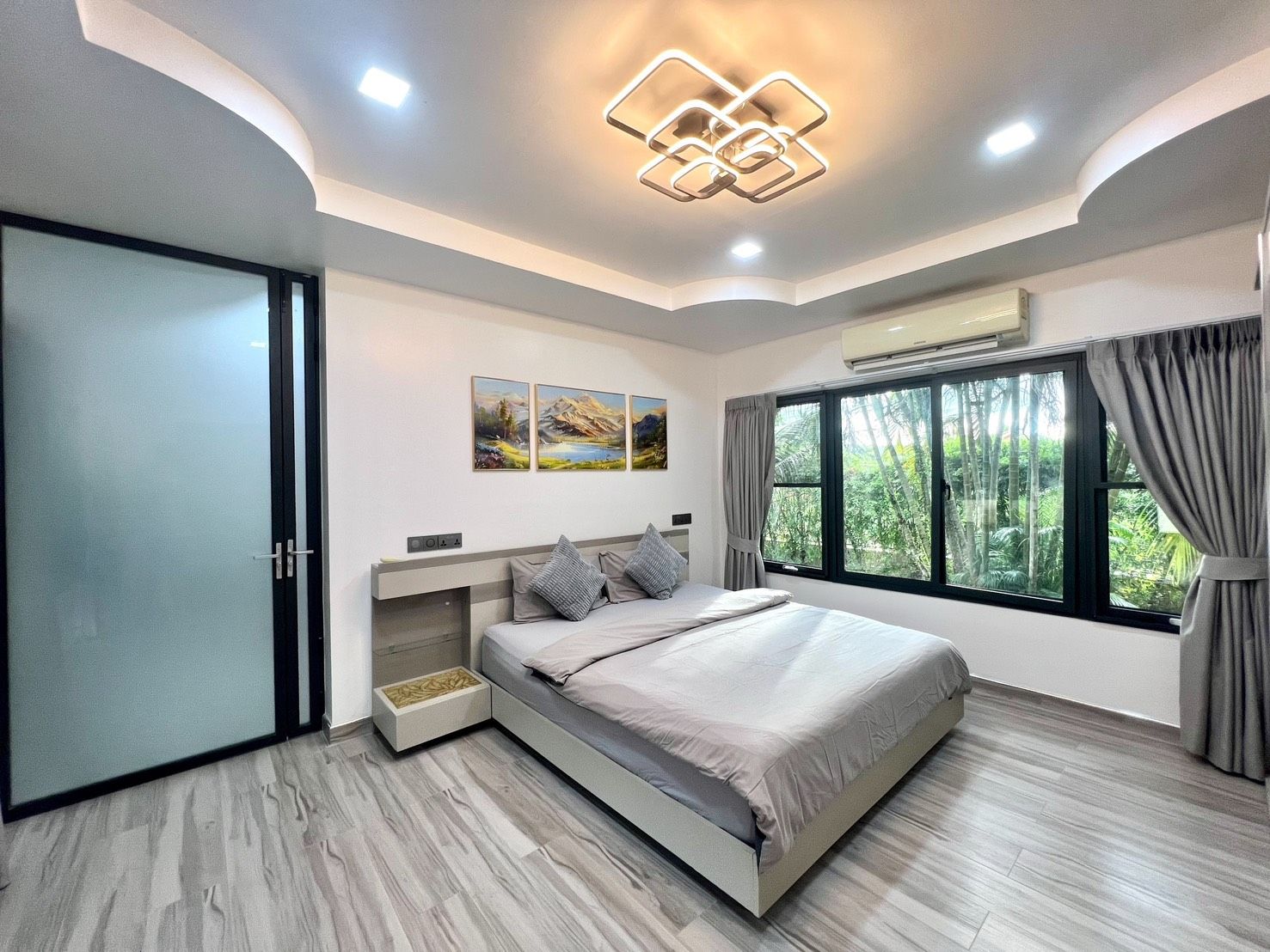 Une chambre moderne avec un lit, une fenêtre avec des rideaux, un climatiseur fixé au mur et un luminaire au plafond.
