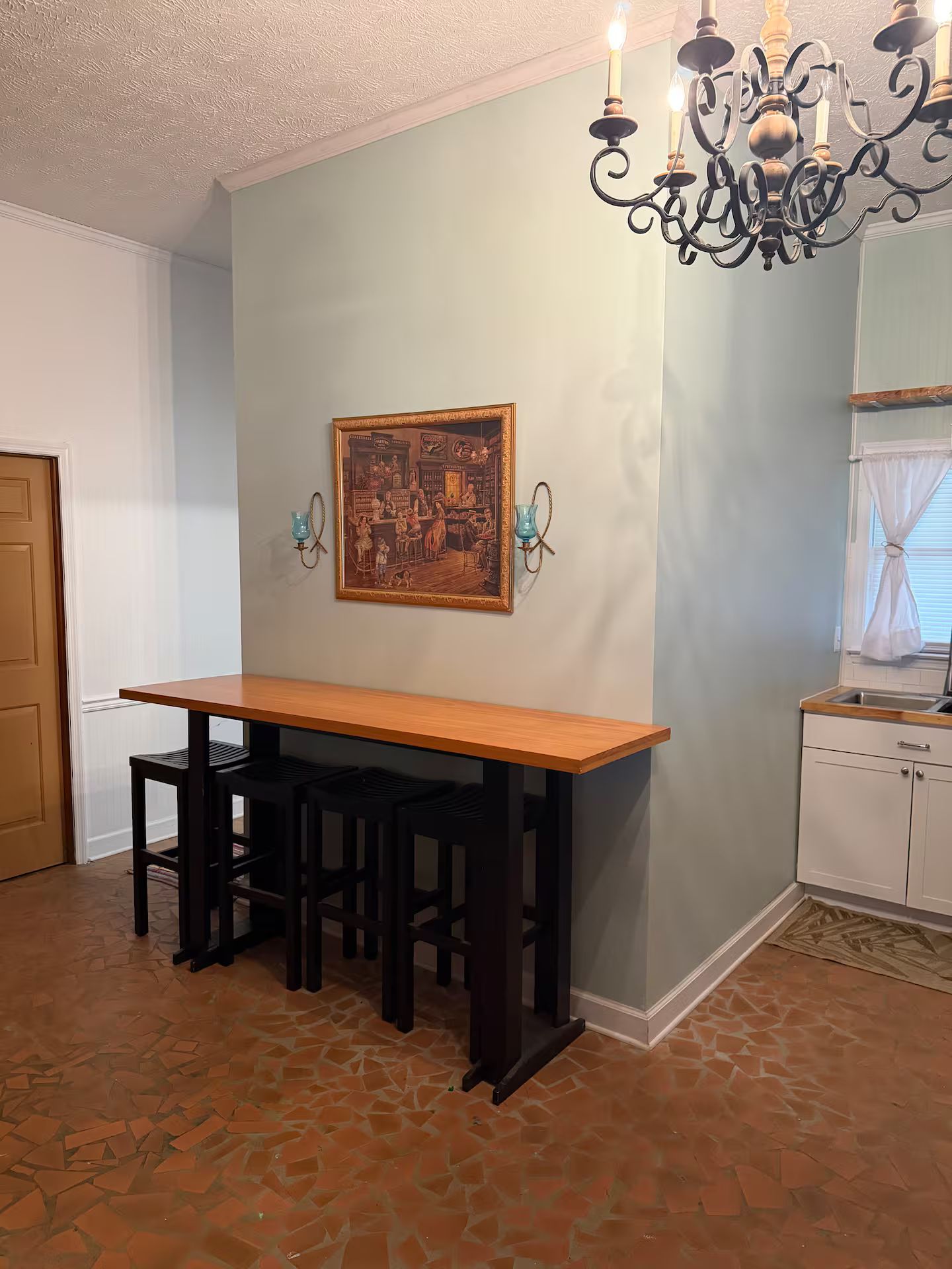 Een eetruimte met een houten tafel, zwarte stoelen, een kroonluchter en een schilderij aan de muur.