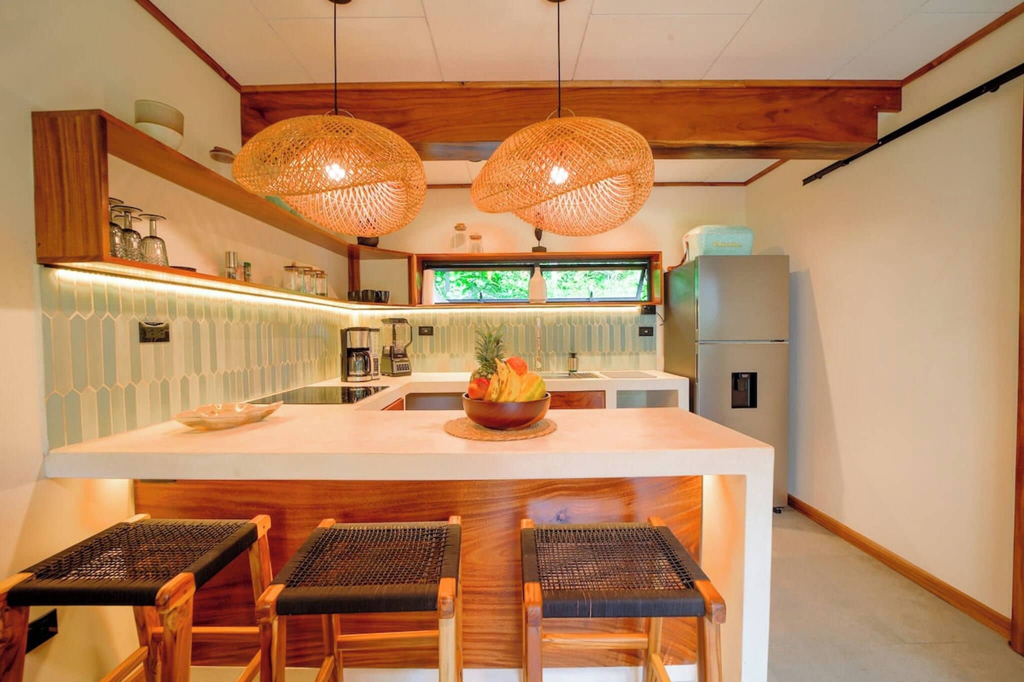 Cozinha moderna com ilha central, cadeiras de madeira e luminárias pendentes.