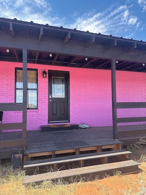 A building with a pink brick exterior, a black door with a star emblem, and a small toy car on the porch.