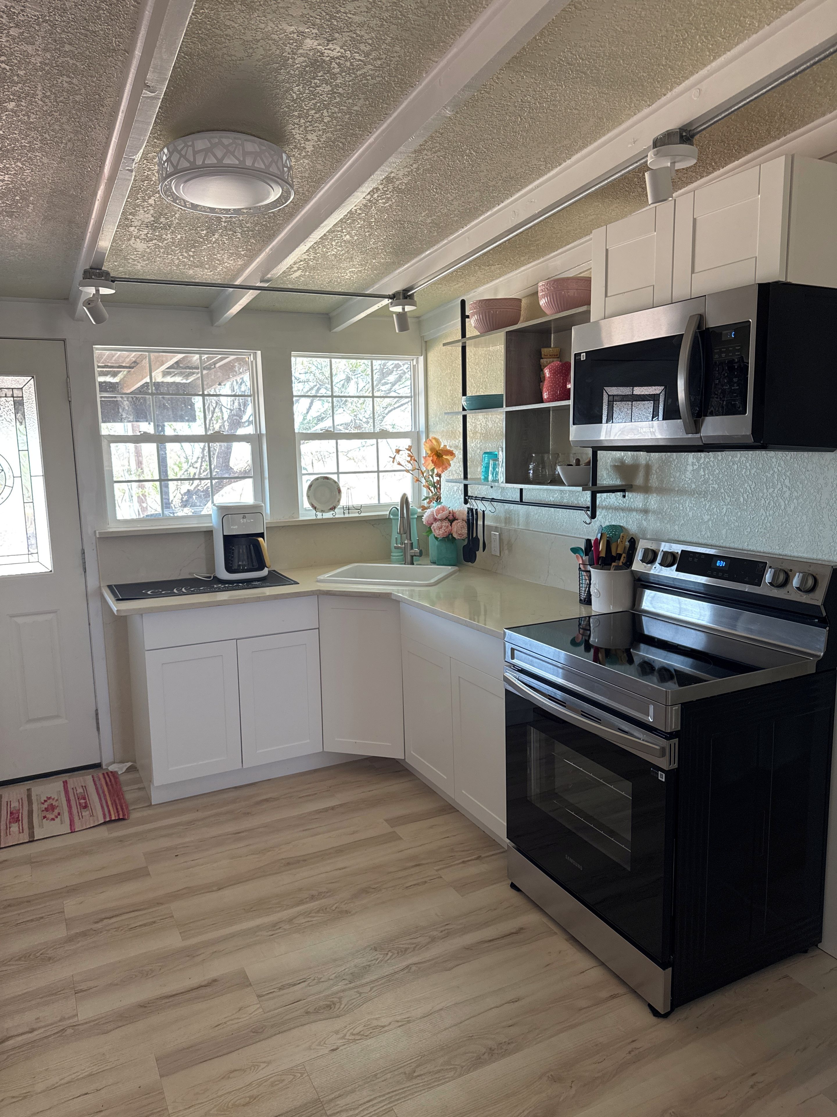 A kitchen with white cabinets, a black stove, a microwave, and a window with a view of trees.