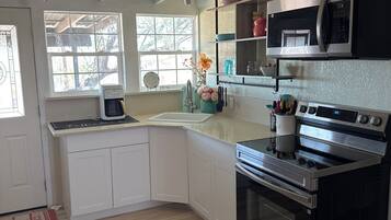 A kitchen with white cabinets, a black stove, a microwave, and a window with a view of trees.