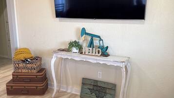 A living room with a flat-screen TV mounted on the wall, a white console table with decorative items, and stacked luggage.