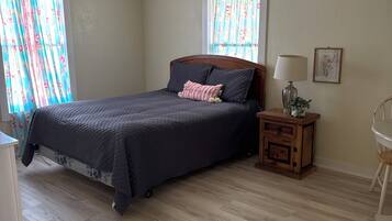 A bedroom with a bed, a ceiling fan, a nightstand with a lamp, and a window with curtains.