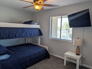 A room with a bunk bed, a ceiling fan, a television, a window with blinds, and a small table with a lamp. - Wonderful 2-bedroom townhome in gorgeous Panama City Beach (Panama City Beach)