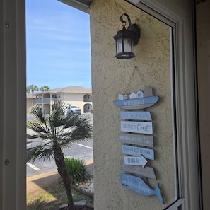 Eine Wand mit einem Schild, auf dem 'BEACH HOUSE' steht, sowie weitere Schilder mit Aufschriften wie 'EIN ORT, WO MAN GUT LANGSAM MACHEN KANN' und 'HERZLICH WILLKOMMEN.'