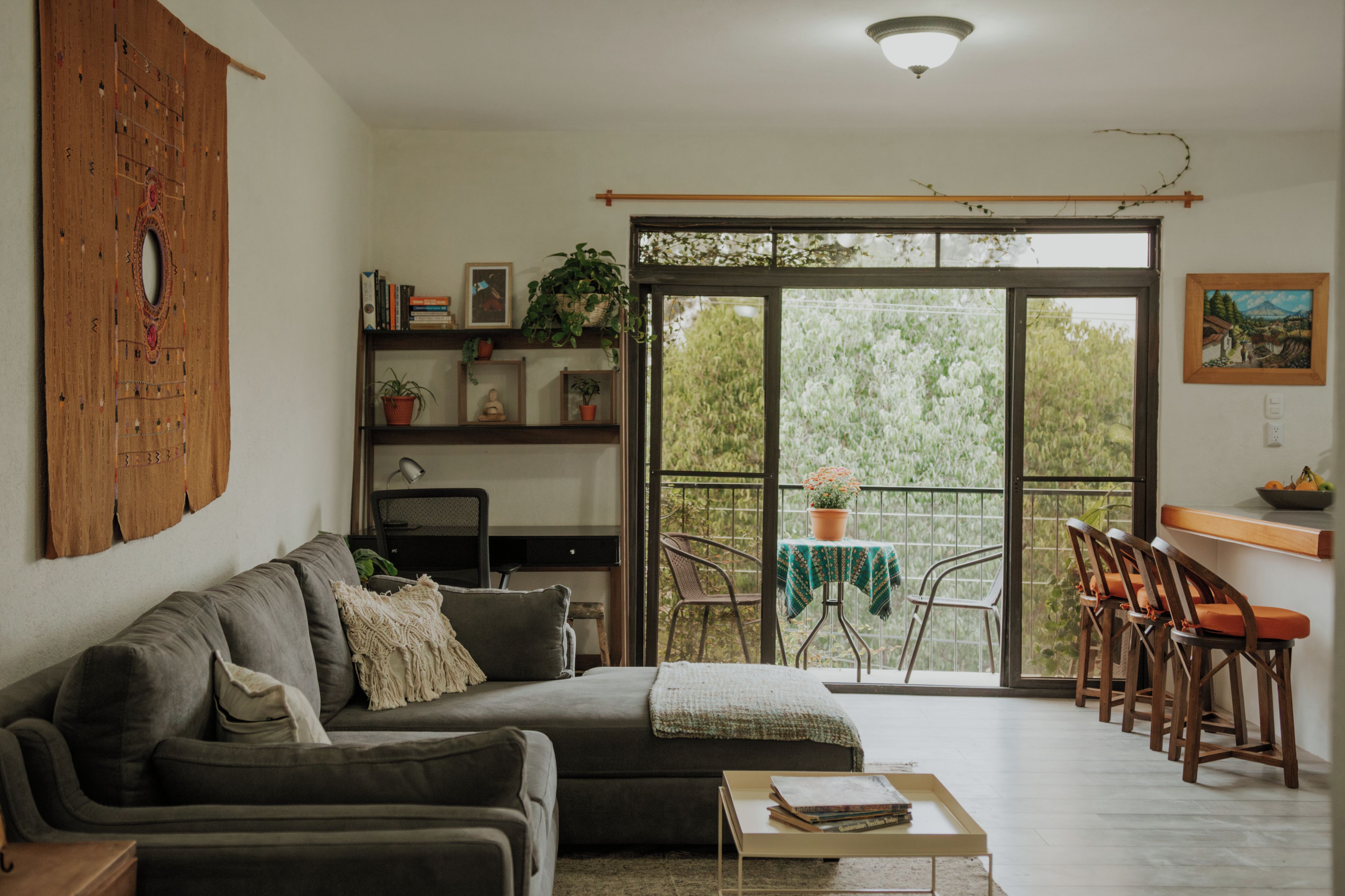 A living room with a sofa, a coffee table, a desk, and a balcony with chairs.