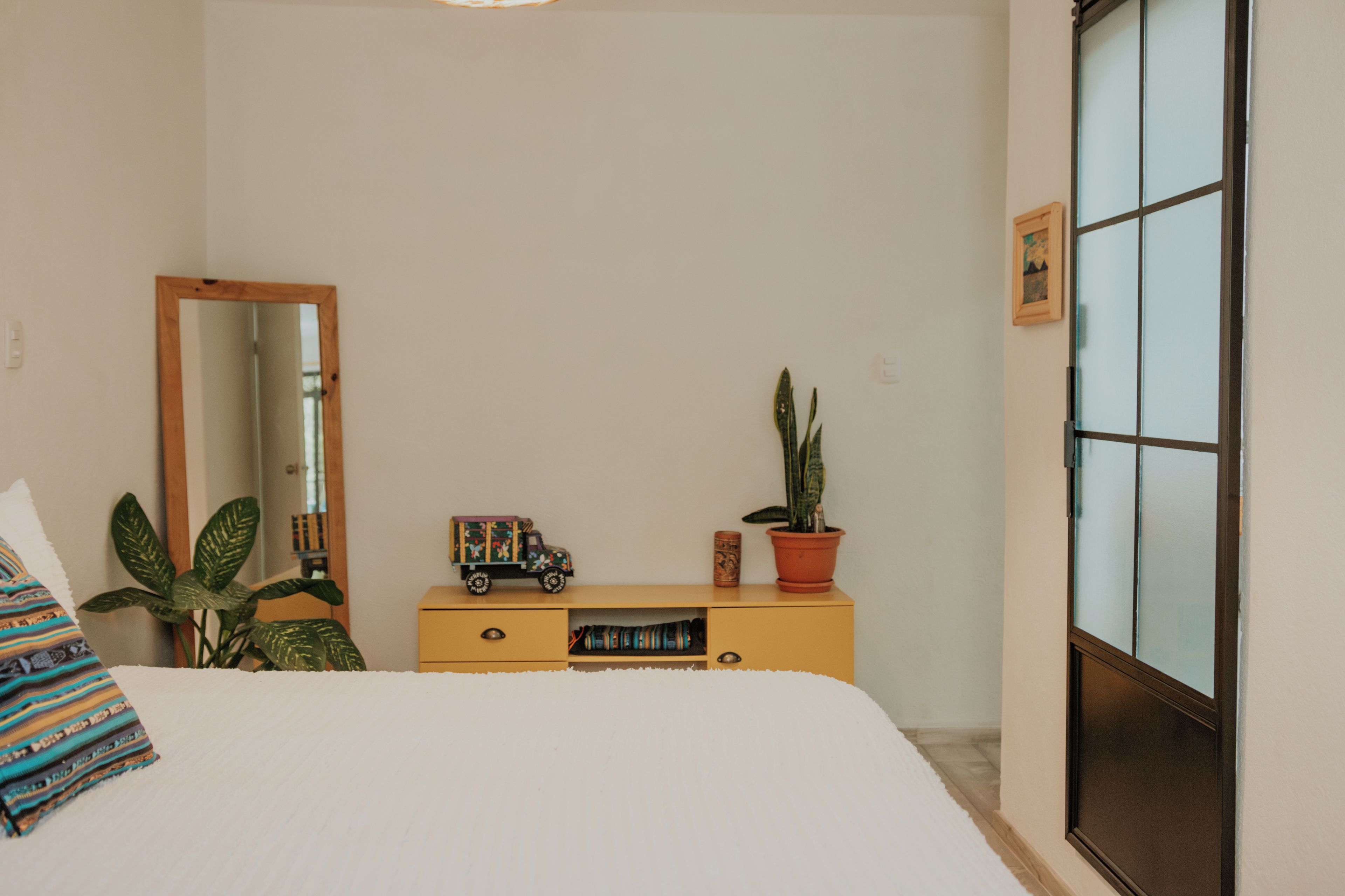 A bedroom with a bed, a dresser, a mirror, a window, and a potted plant.