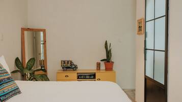A bedroom with a bed, a dresser, a mirror, a window, and a potted plant.