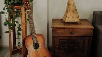 A guitar on a stand, a wooden nightstand with a decorative item, and a hanging plant.