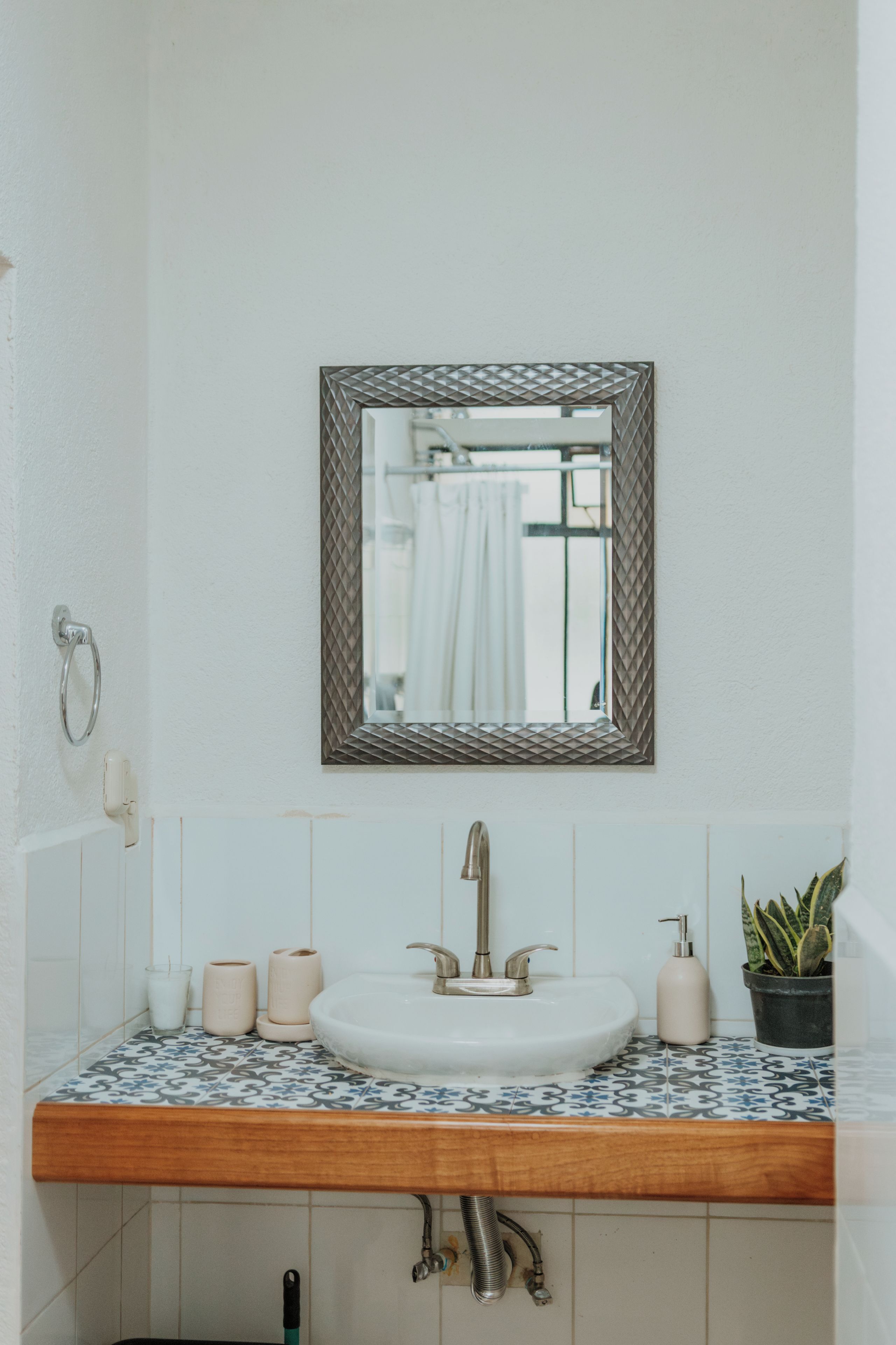 A bathroom with a white sink, a mirror with a geometric frame, and a potted plant.