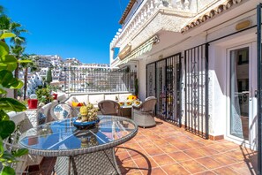 A terrace with a glass table and wicker chairs, overlooking a cityscape. - Holiday Home in Nerja With Sea Views (Nerja)