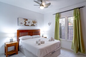 A hotel room with a bed, two bedside lamps, a ceiling fan, a window with green curtains, and a decorative wall piece. - Holiday Home in Nerja With Sea Views (Nerja)