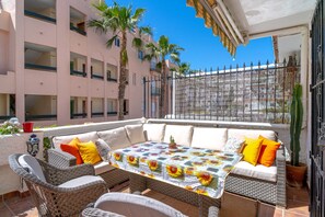 A sunlit outdoor seating area with wicker furniture, a table with a floral tablecloth, and a cactus plant. - Holiday Home in Nerja With Sea Views (Nerja)