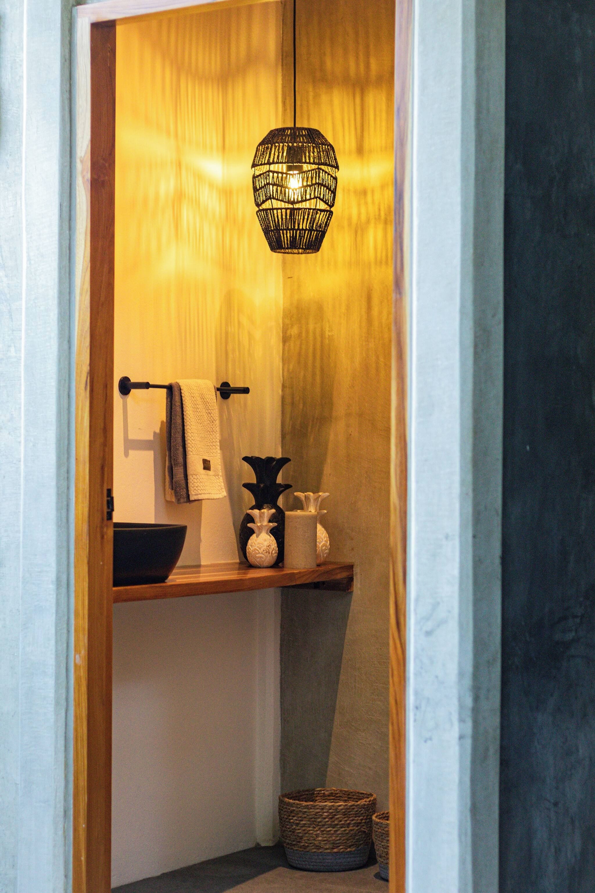 Un baño con puerta de madera, perchero, lavamanos, un jarrón decorativo y una lámpara colgante.