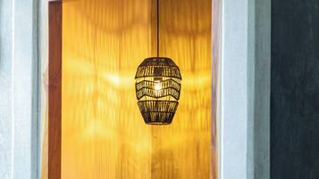 Un baño con puerta de madera, perchero, lavamanos, un jarrón decorativo y una lámpara colgante.