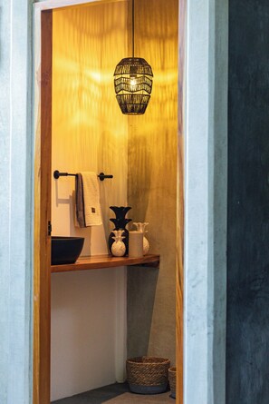 Un baño con puerta de madera, perchero, lavamanos, un jarrón decorativo y una lámpara colgante.