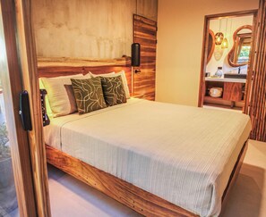 Ein Bett mit Holz-Kopfstück, zwei Kissen mit Blattmuster und ein Nachttisch mit Lampe.