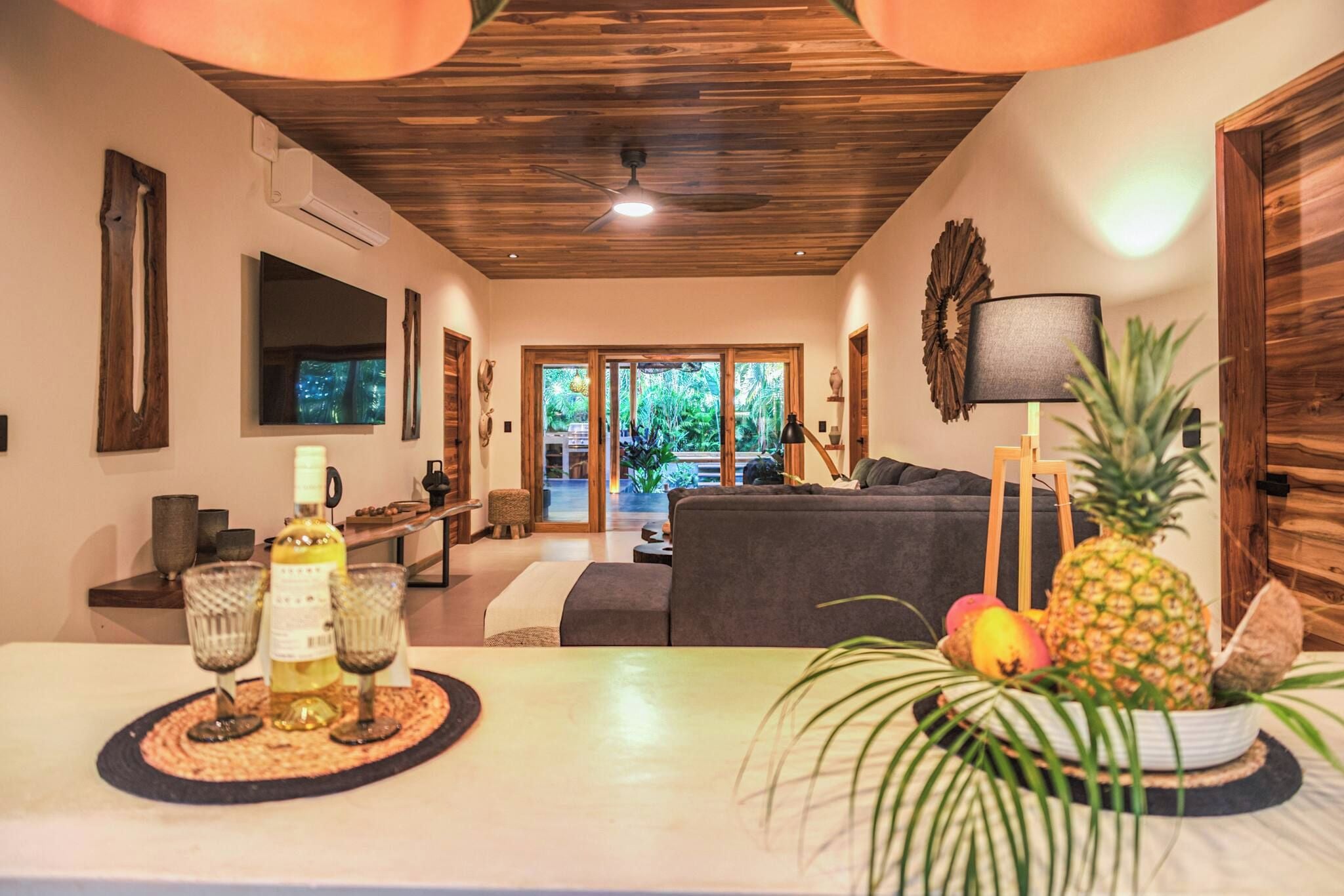 Una sala moderna con techo de madera, un sofá, una mesa de centro con bebidas y vista al exterior.