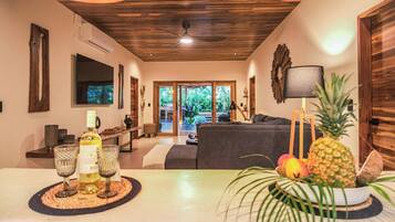 Una sala moderna con techo de madera, un sofá, una mesa de centro con bebidas y vista al exterior.