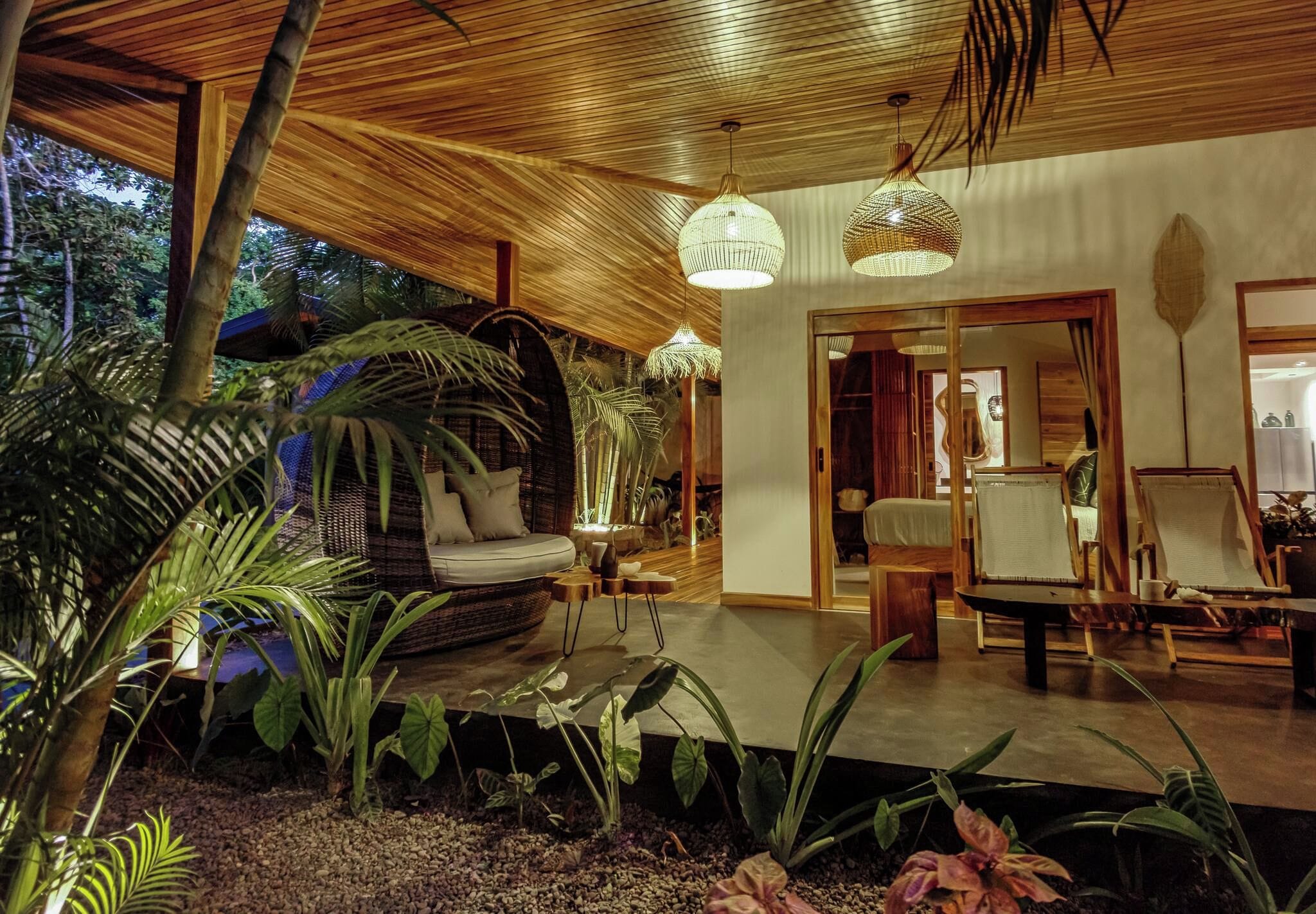 A tropical-themed interior with a wooden ceiling, a cushioned seating area, and a variety of plants.