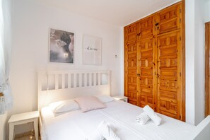 A bedroom with a white bed, a wooden wardrobe, and two framed pictures on the wall. - Holiday Home in Nerja With Sea Views (Nerja)
