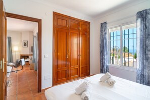 A hotel room with a large bed, a wooden wardrobe, a window with a view, and a bathroom visible in the background. - Villa in Tamango Hill Near Playa Guilche (Nerja)