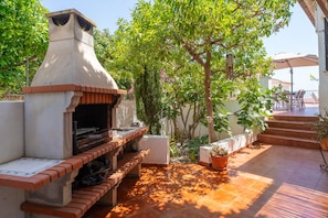 An outdoor patio with a brick barbecue grill, surrounded by potted plants and a tiled floor. - Villa in Tamango Hill Near Playa Guilche (Nerja)
