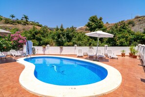 A swimming pool with a curved edge, surrounded by lounge chairs and umbrellas, with a view of hills and vegetation in the background. - Villa in Tamango Hill Near Playa Guilche (Nerja)