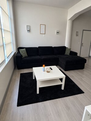 A modern living room with a black sectional sofa, a white coffee table, and a black rug. There are two wall-mounted lights and a framed picture on the wall. - Luxury Cincinnati Getaway Modern, Stylish & Spacious (Cincinnati)