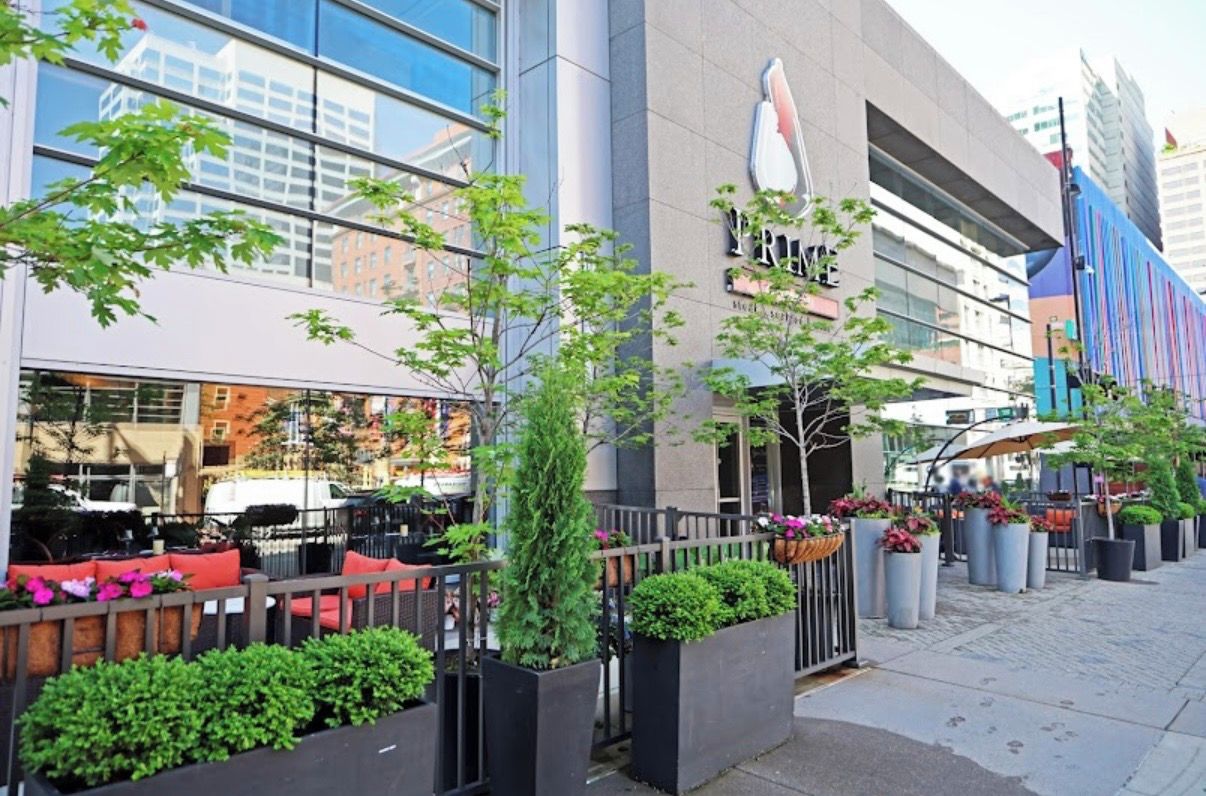 A modern building with a glass facade, outdoor seating, and potted plants.
