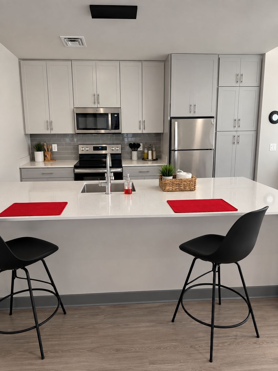 A modern kitchen with white cabinets, stainless steel appliances, and a central island with two black bar stools.
