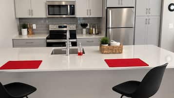 A modern kitchen with white cabinets, stainless steel appliances, and a central island with two black bar stools.