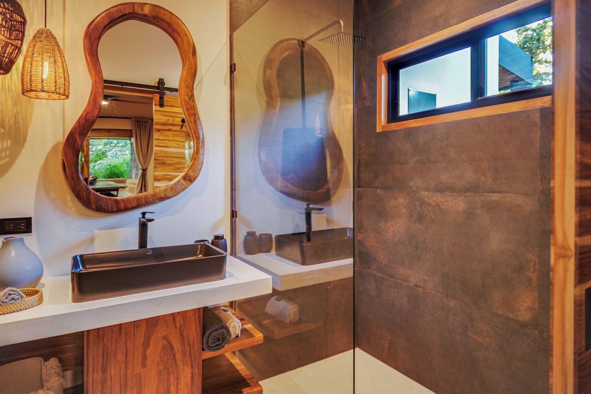 Un baño con tocador de madera, un espejo grande, ducha moderna y ventana con vistas.