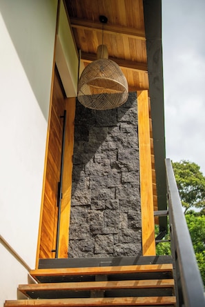 Escadaria com parede de pedra e detalhes em madeira, levando a um quarto com luminária pendente.