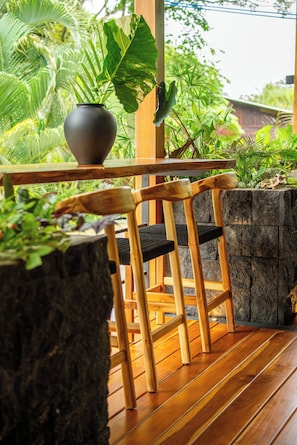 A wooden outdoor seating area with chairs and a table, surrounded by large potted plants and a stone wall. - Retreat Villa Wabi Sabi Umi (Cahuita)