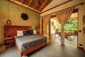 Un dormitorio con cama de madera, una mesita de noche, una lámpara colgante y vistas a un área de comedor exterior.