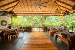 A spacious indoor area with a wooden floor, a ceiling fan, and a view of lush greenery outside. - Retreat Villa Wabi Sabi Umi (Cahuita)