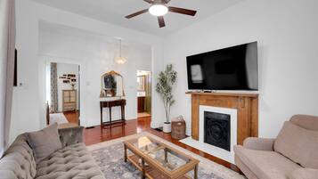 A living room with a fireplace, a television, and a ceiling fan.