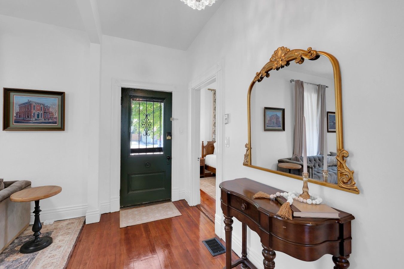 A hallway with a green door, a large mirror, a wooden console table, and a framed picture on the wall.