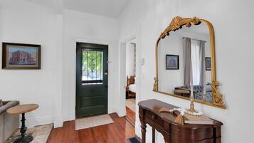 A hallway with a green door, a large mirror, a wooden console table, and a framed picture on the wall.