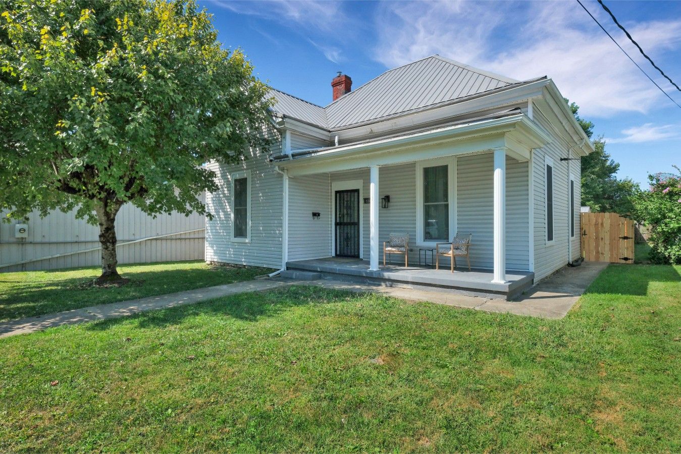 A single-story house with a front porch, a tree in the yard, and a wooden fence.
