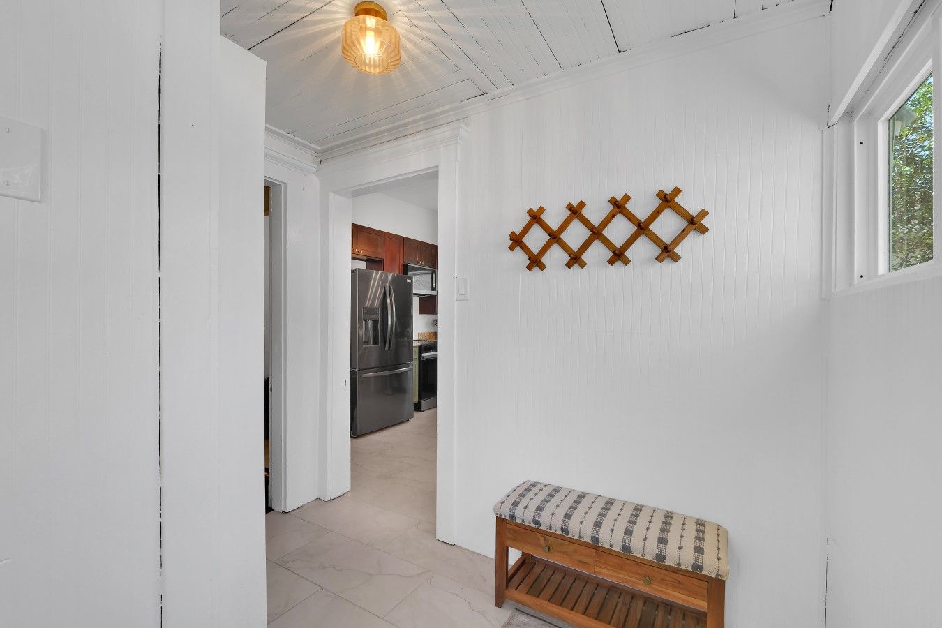 A hallway with a bench, a wooden wall decoration, and a kitchen in the background.