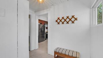 A hallway with a bench, a wooden wall decoration, and a kitchen in the background.