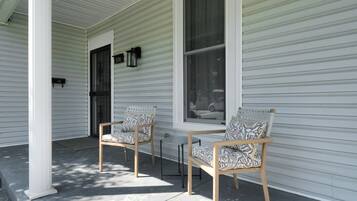 A porch with two wooden chairs and a table, white siding, and a window.