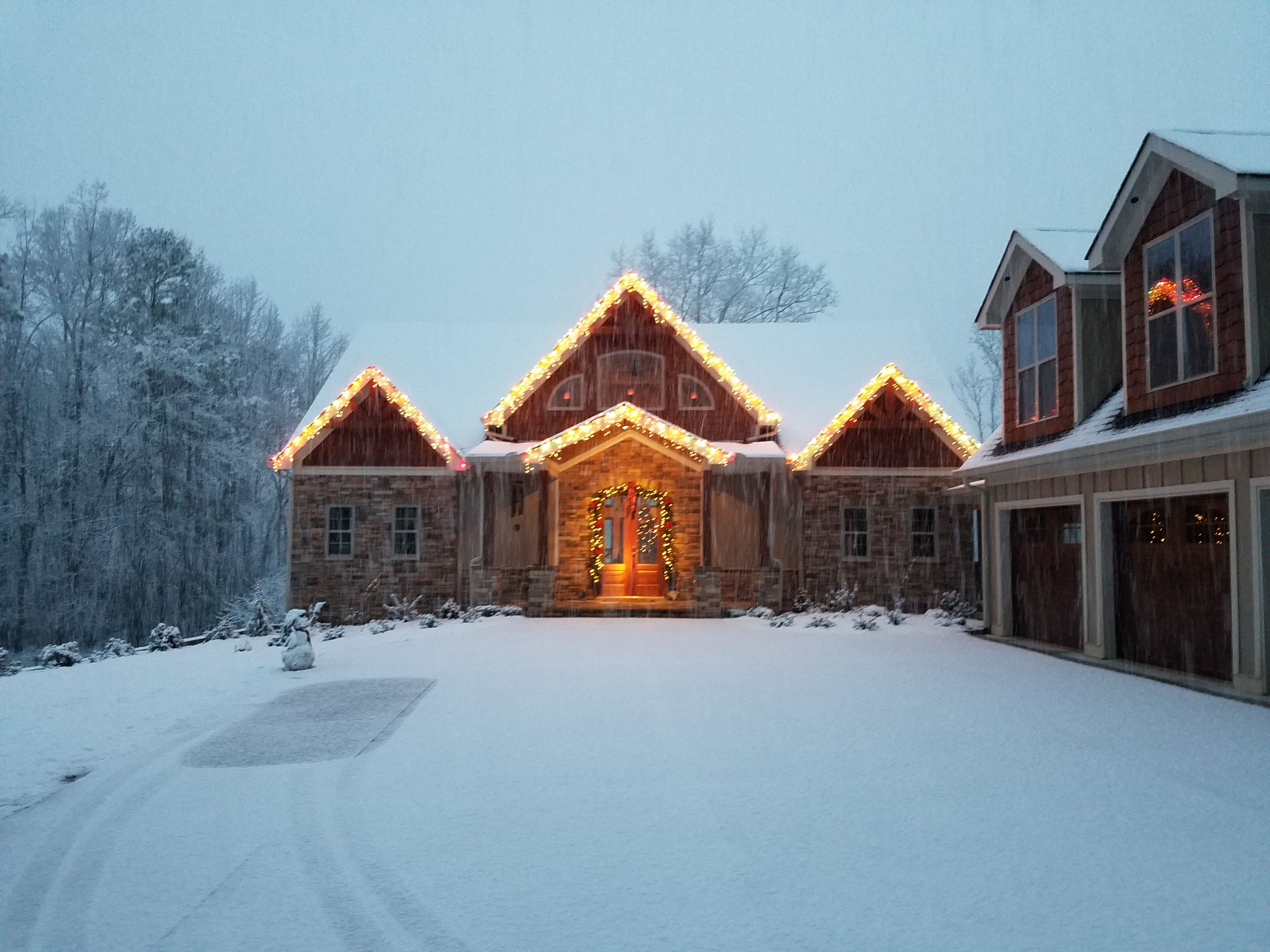A stone house with a snow-covered driveway and a garage.